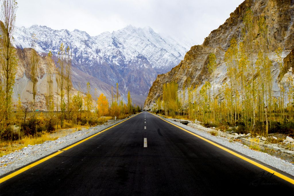 Beautiful road in Hunza Valley surrounded by autumn trees and snow-covered mountains.