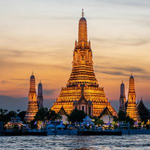 A captivating view of Wat Arun Temple illuminated at sunset along the Bangkok riverside.