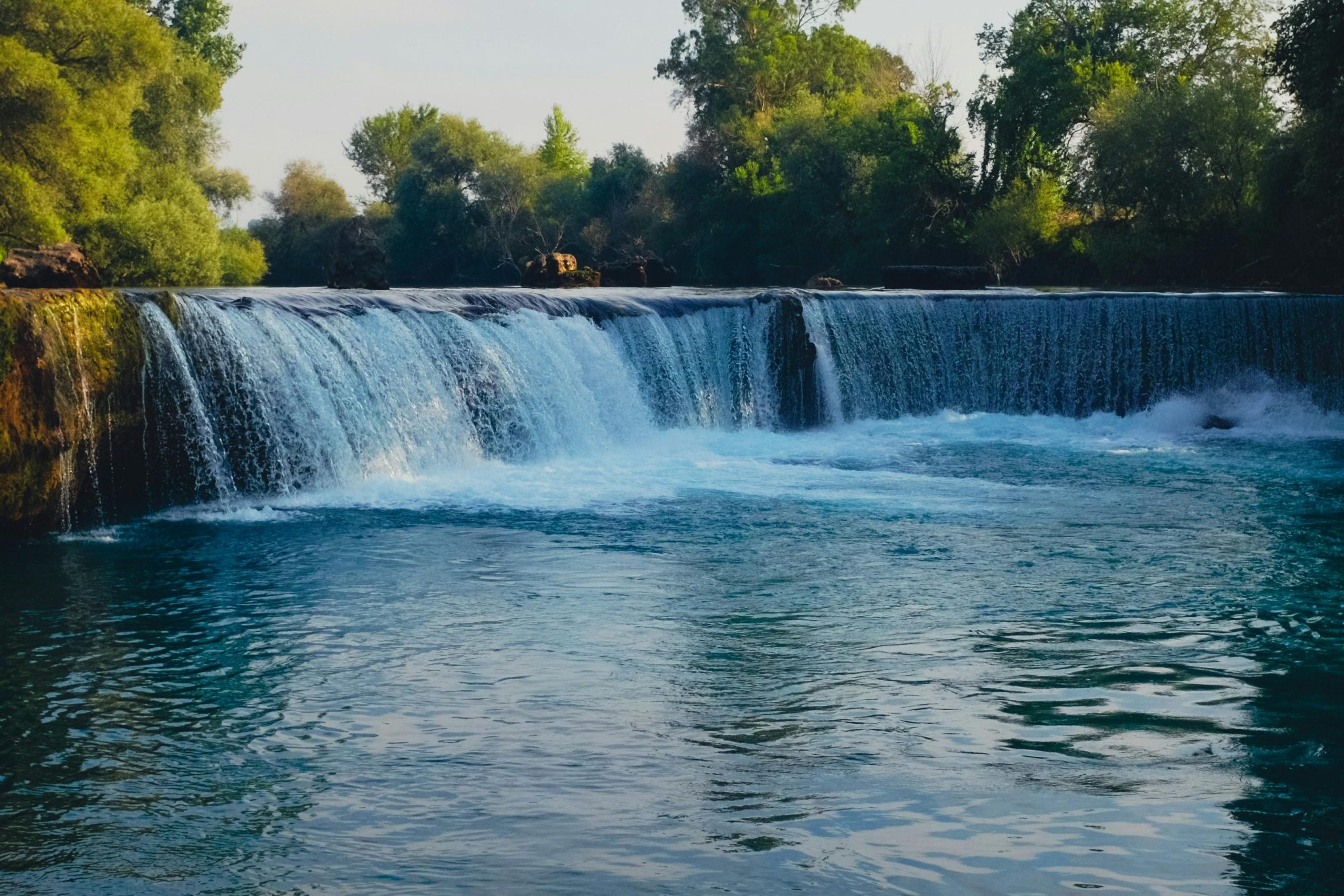 A tranquil waterfall cascading into a river surrounded by lush greenery, captured in natural daylight.