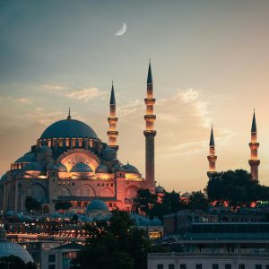 Suleymaniye Mosque illuminated in Istanbul at dusk, showcasing its Ottoman architecture under a crescent moon.